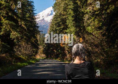 Eine weißhaarige Frau beobachten die Landschaft von Baker Lake Road mit Mount Baker im Hintergrund in North Cascades geschneit Stockfoto