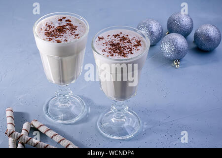 Zwei selbstgemachte Eierlikör Milchshakes mit Zimt, Weihnachten Dekorationen auf einem blauen Hintergrund. Weihnachtliche Atmosphäre. Stockfoto
