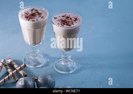 Zwei selbstgemachte Eierlikör Milchshakes mit Zimt, Weihnachten Dekorationen auf einem blauen Hintergrund. Weihnachtliche Atmosphäre. Stockfoto