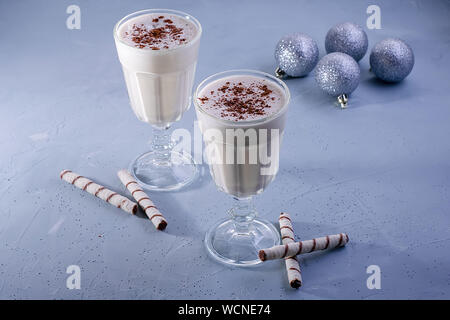 Zwei selbstgemachte Eierlikör Milchshakes mit Zimt, Weihnachten Dekorationen auf einem blauen Hintergrund. Weihnachtliche Atmosphäre. Stockfoto