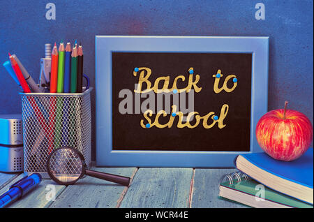 Schreibwaren, Schulbücher, Notebooks, Apple und Papier Text "Zurück in die Schule" auf der Tafel Stockfoto