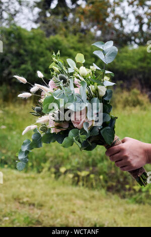 Hand, die einer Frau einen Brautstrauß mit frischen weißen und rosa Blüten Stockfoto
