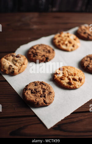 Schokolade Cookies auf einem Pergament Papier in einer Reihe. Glutenfreie Plätzchen auf einer hölzernen Tisch aus dem Backofen. Selektiver Fokus Stockfoto