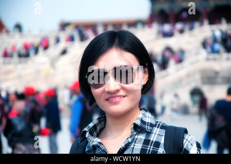 Einen lächelnden chinesischen Frau Sonnenbrillen tragen, einen Rucksack und schwarz-weiß karierten Hemd in der Verbotenen Stadt in Peking, China. Stockfoto