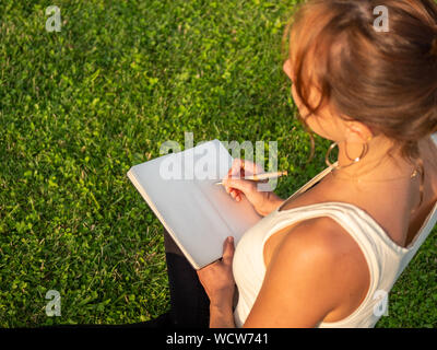 Nahaufnahme der Geschäftsfrau im grünen Gras sitzen und schreiben Termine im Kalender Tagebuch Stockfoto