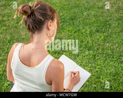 Nahaufnahme der Geschäftsfrau im grünen Gras sitzen und schreiben Termine im Kalender Tagebuch Stockfoto
