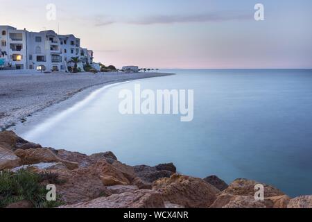 Lange Belichtung Mittelmeer, Strand mit weißen Felsen, weißes Hotel und Vordergrund Felsen in Marina, Port El Kantoui, Tunesien, während blaue Stunde Stockfoto