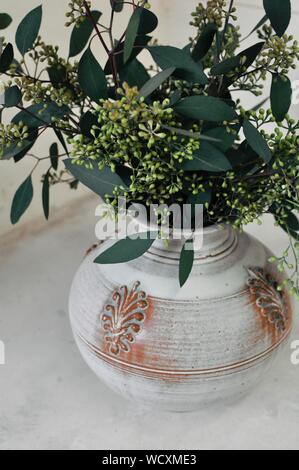 Vertikale Nahaufnahme von grünen Blumen und Blättern in einem Weiße Vase Stockfoto