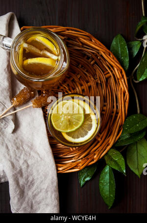 Blick von oben auf die Tasse Tee mit frischen Zitronen und Limetten, brauner Zucker Sticks und grünen Pflanzen auf rustikalen Hintergrund. Stockfoto