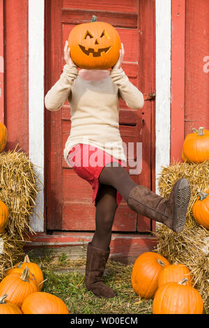 Fröhlicher, verspielter Junge Frau Spaß im Freien im Herbst. Sie hält eine Kürbis Jack-o-Lantern vor ihrem Gesicht und treten auf die Füße. Stockfoto