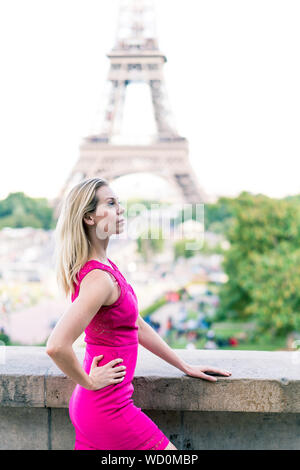 Paris, Frankreich, 2. Juli 2017: junge blonde Frau mit rosa Kleid stehend, Eiffel Turm im Hintergrund Stockfoto