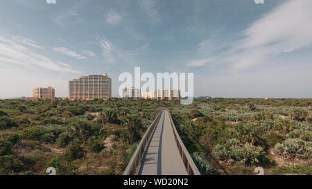 New Smyrna Dunes Park in New Smyrna Beach, Florida. Promenade zum Strand durch Dünen und Scheuern. Eigentumswohnungen in tha Hintergrund. Stockfoto