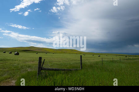 Dramatische Sturm Wolken über eine Weide mit runde Heuballen und einen Zaun im Vordergrund. Stockfoto