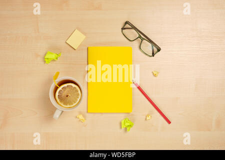 Gelber Notizblock mit roten Bleistift, Tasse Kaffee und Gläser liegen auf einem hellen Holz- Tabelle durch die zerknitterten Blätter umgeben. Stockfoto