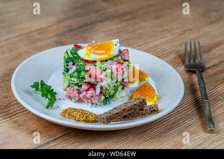 Lecker Salat mit Broccoli, Tomaten, Zwiebeln und gekochtem Ei mit Sahne Soße in eine Platte auf Holz- Hintergrund. Gesundes Essen, in der Nähe Stockfoto