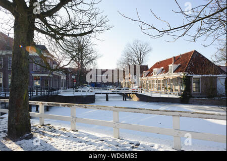 Gefrorenes Wasser und Show auf den Kanal und die traditionellen alten Backsteinbauten mit Ziegeldächern am sonnigen Wintertag in Makkum, Holland Krone, Niederlande. Stockfoto