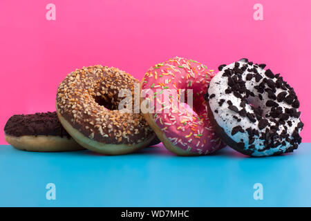Vier verschiedene Krapfen stehen auf einem blau und rosa Hintergrund Nahaufnahme Stockfoto