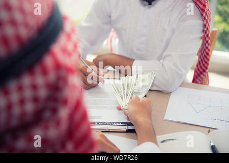 Unternehmer 1001 unterzeichnen Vertrag und Exchange zusammen Geld am Tisch Büro Arbeitsplatz, Nahaufnahme der arabischen Geschäftsleuten in traditioneller Kleidung ar Stockfoto