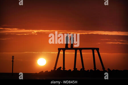 Die Sonne über die Skulptur "Das Paar" vom Künstler Sean Henry, in Newbiggin-by-the-Sea in Northumberland. Stockfoto