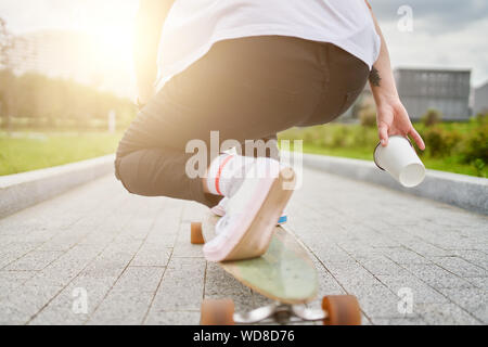 Foto der Beine der Frau in weißen Turnschuhen, Skateboard fahren auf der Straße in der Stadt im Sommer Tag. Sonnenlicht Wirkung Stockfoto