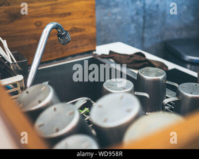 Close-up Stapel aus Aluminium Becher auf Aluminium Küche Waschbecken mit Wasserhahn im Cafe. Stockfoto