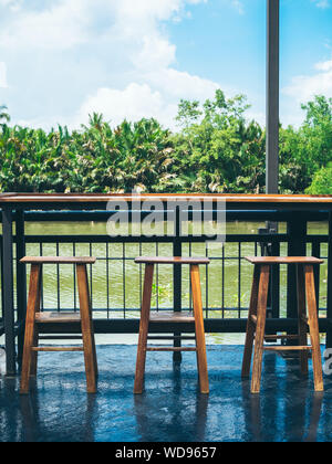 Leere Holz Barhocker und Holz- Bar auf der Terrasse mit Blick auf den Fluss vertikalen Stil. Stockfoto