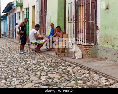 TRINIDAD, Kuba - May 05, 2013: Eine Gruppe von afrikanischen amerikanischen Männer spielen ein Brettspiel rund um einen Tisch auf der Straße mit Kopfsteinpflaster in der Nähe von einem Hund Stockfoto