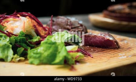 Nahaufnahme eines Tellers mit Fleisch und Gemüseblättern auf Ein Holztablett mit unscharfem Hintergrund Stockfoto