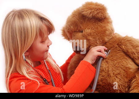 Blonde Mädchen mit einem Stethoskop zu ihren großen braunen Teddybären Herz. Stockfoto