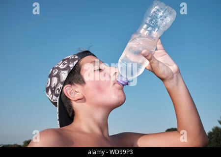 Junge, 11-12 Jahre alt, Getränke eiskaltes Wasser aus der Plastikflasche an einem heißen Sommertag Stockfoto