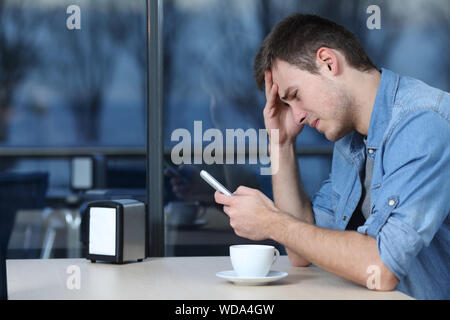 Seitenansicht Porträt einer traurigen Mann Kontrolle Handy Nachricht in einem Coffee Shop Stockfoto