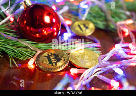 Weihnachtsdekor Bitcoins, Kugel auf einem Holzbrett mit Kiefernzweigen und Urlaub. Münzen bitcoin unter dem Zweig von einem Weihnachtsbaum, auf der Stockfoto