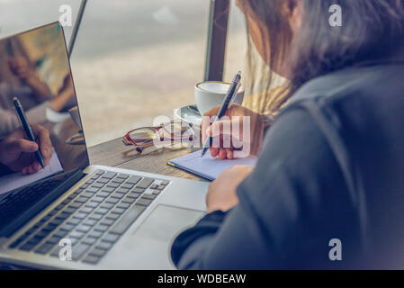 Seitenansicht der asiatischen Frau schreiben Notebook neben Laptop Stockfoto
