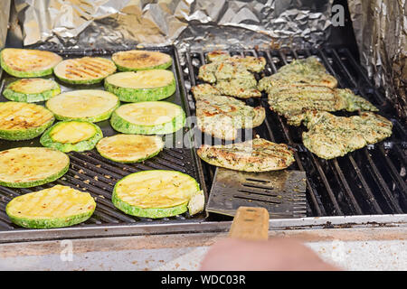 Mann kochen Steaks und Zucchini Medaillons sind auf Gas-Grill Gitter gekocht, first person View Konzept unsachgemäße Kochen Fleisch auf dem Grill Stockfoto