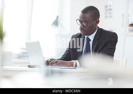 Afrikanische Mann bei seiner Arbeit im Büro saß er am Tisch, und geben Sie auf dem Computer konzentrieren. Stockfoto