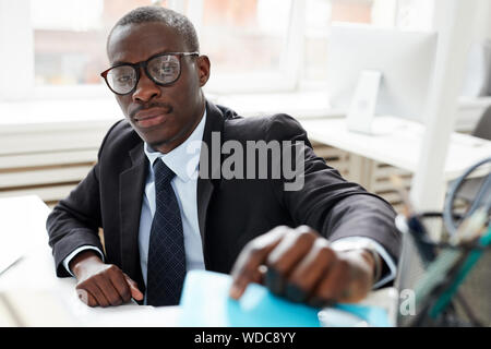Schweren afrikanischen Geschäftsmann in Brillen und besetzt mit seiner Arbeit am Tisch im Büro Stockfoto