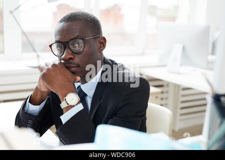 Portrait von zuversichtlich Afrikanischen Geschäftsmann in Brillen am Tisch mit nachdenklichen Augen saßen und an Kamera Stockfoto