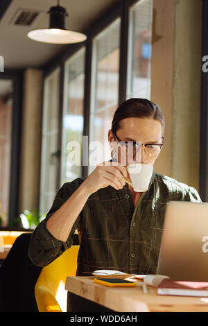 Angenehmer netter Mann Kaffee trinken während seiner Arbeit Stockfoto