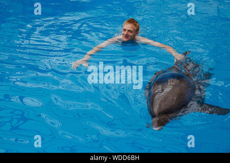 Glückliche Menschen schwimmen mit Delfin im Delphinarium Stockfoto