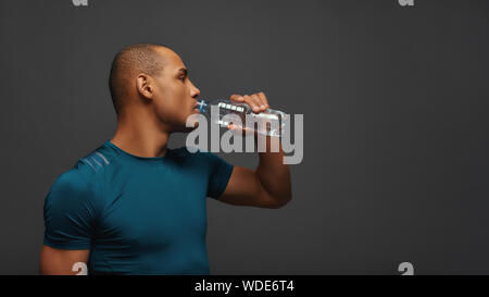 Portrait des jungen Mannes tragen Sportswear Trinkwasser beim Stehen über grauer Hintergrund isoliert. Fitness- und Arbeit Konzept vor. Horizontale erschossen. Seitenansicht Stockfoto