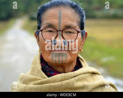 Ältere indische Apatani tribal Frau mit schwarzem Holz- nase Stopfen (yaping hullo) und unverwechselbares Gesicht Tribal Tattoo posiert für die Kamera. Stockfoto