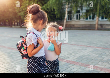 Glückliche Schwestern Mädchen, Rucksäcke und Spaß haben. Kinder, Schüler gehen nach dem Unterricht im Freien Grundschule. Bildung. Zurück zur Schule Stockfoto