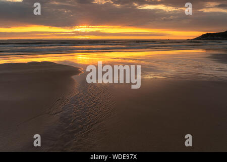 Surfer genießen Sie die Wellen am Strand auf combesgate North Devon bei Sonnenuntergang. Stockfoto