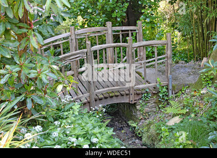Ein altes rustikales Zaun über einen dünnen Strom in einem englischen Country Garden in Devon, England Stockfoto