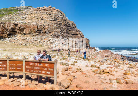 Paar für ein Foto von dem Schild am Kap der Guten Hoffnung, die am südwestlichen Punkt auf dem afrikanischen Kontinent, Western Cape, Südafrika posing Stockfoto