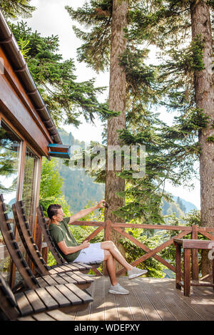 Junger Mann in Bergen im tollen Restaurant mit Blick auf die Sommerferien. Wunderschöne Landschaft Stockfoto