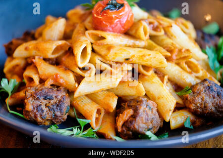 Penne Nudeln mit Hackfleischbällchen in Tomatensauce in einem schwarzen Schüssel Stockfoto