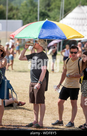 Ein Mann von Trinkwasser mit einem improvisierten Sonnenschirm am Glastonbury Festival 2019 in Pilton, Somerset Stockfoto