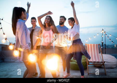 Gerne Freunde mit Getränken Schiebeschalter auf der Dachterrasse bei Nacht Stockfoto