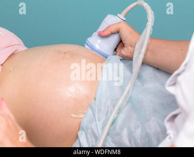 Sonograph Scannen der jungen schwangeren Bauch mit Ultraschallsensor, Geburtshilfe oder Schwangerschaft Ultraschall Verfahren Stockfoto